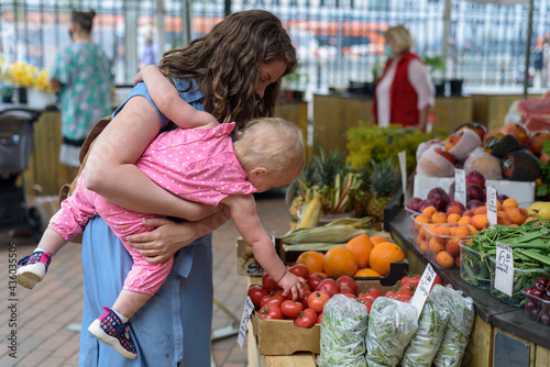 Woman buying vegetables with baby girl on farmers food market