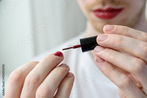Bearded man with red lipstick on his lips applying nail polish