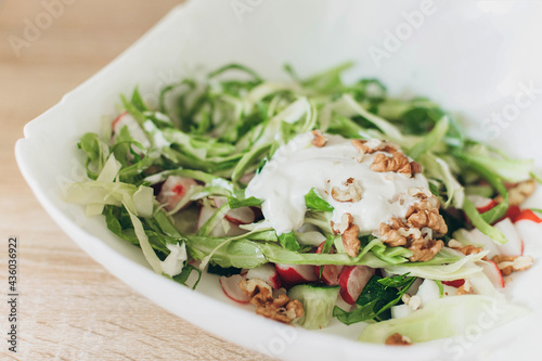 Summer vegetable salad with fresh cabbage radishes, walnuts, sour cream on a white plate