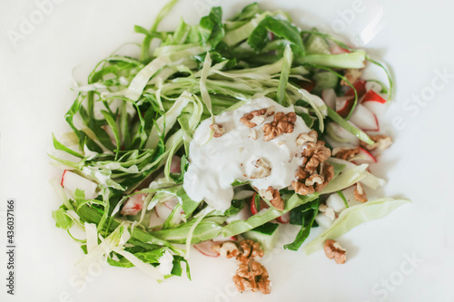 Summer vegetable salad chopped with fresh cabbage radishes, walnuts, sour cream on a white background 