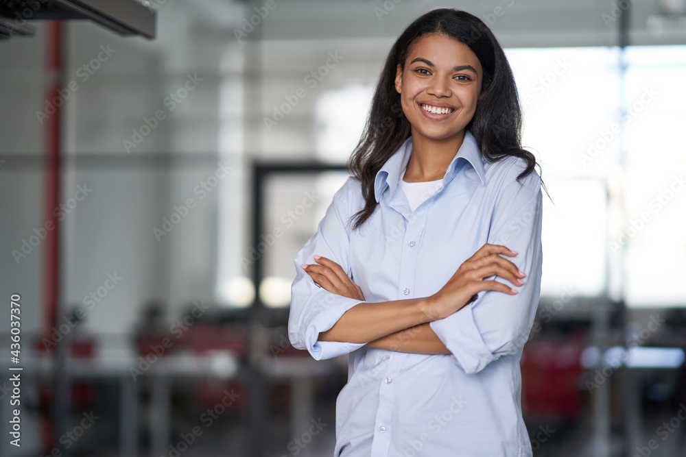 Portrait of a young happy attractive business woman or female office worker keeping arms crossed, looking at camera and smiling while working in the modern office Portrait of a young happy attractive business woman or female office worker keeping arms crossed, looking at camera and smiling while working in the modern office