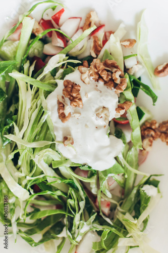 Summer vegetable salad chopped with fresh cabbage radishes, walnuts, sour cream on a white background 
