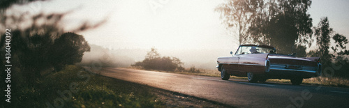 Canvastavla A retro car drives along the road at dawn