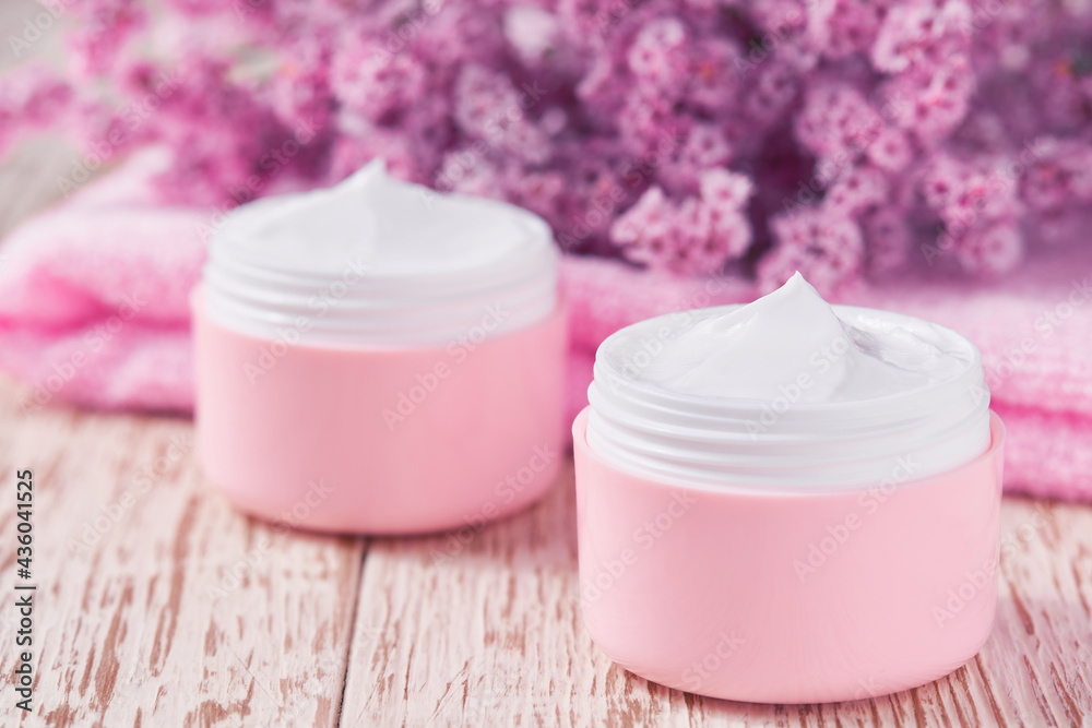Natural face cream or lotion, organic cosmetic product to moisturize the skin with a towel and flowers on the background. Pink series cosmetic. Natural face cream or lotion, organic cosmetic product to moisturize the skin with a towel and flowers on the background. Pink series cosmetic.