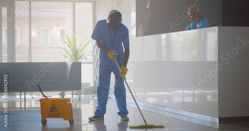 Bild auf Leinwand Afro-american janitor in headphones washing floor in hospital reception area