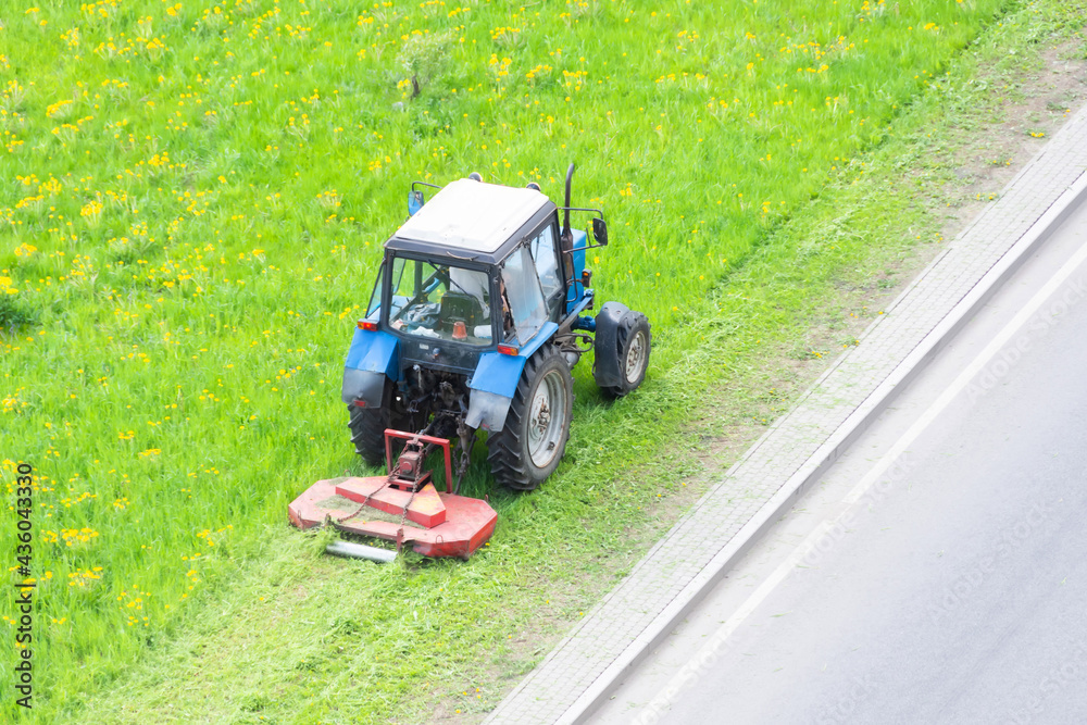 Tractor uses trailed lawn mower to mow grass on city lawns, aerial view. Tractor uses trailed lawn mower to mow grass on city lawns, aerial view.