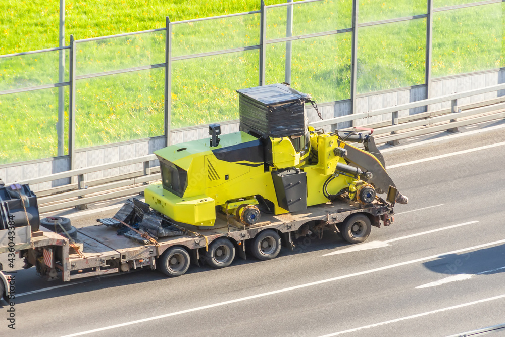 Truck with a long trailer platform for transporting heavy machinery, loaded tractor without wheels and bucket. Highway transportation.