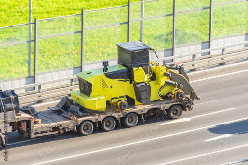 Truck with a long trailer platform for transporting heavy machinery, loaded tractor without wheels and bucket. Highway transportation. © aapsky