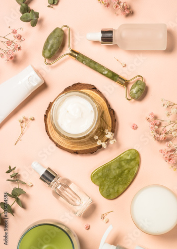Cosmetic products - Jade roller and gua sha massager with cream and serum bottles at pastel background. Spa background. Top view with copy space.