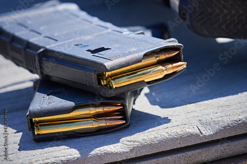 AR15 Rifle Magazines stacked sitting next to a carbine rifle on a table at an outdoor shooting range. 