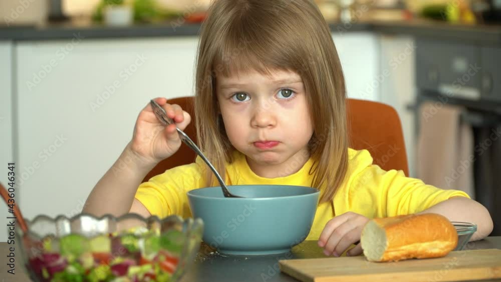 Little 4 year old girl eats with spoon tomato soup puree with croutons and cheese on kitchen. Close up of kid has lunch. Food concept Little 4 year old girl eats with spoon tomato soup puree with croutons and cheese on kitchen. Close up of kid has lunch. Food concept