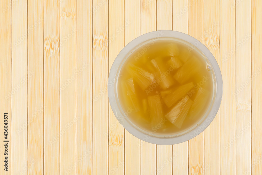 Plastic container filled with diced pineapple in natural juice on a wood tabletop. Plastic container filled with diced pineapple in natural juice on a wood tabletop.