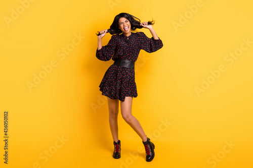 Full size photo of young happy excited crazy funky girl hold hair tails showing tongue isolated on yellow color background