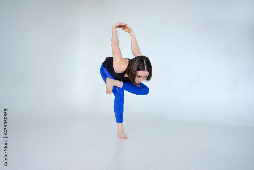 Portrait of sporty woman doing Kapotasana or standing Pigeon Pose. Attractive young woman training yoga on white background isolated on cyclorama. Portrait of sporty woman doing Kapotasana or standing Pigeon Pose. Attractive young woman training yoga on white background isolated on cyclorama.