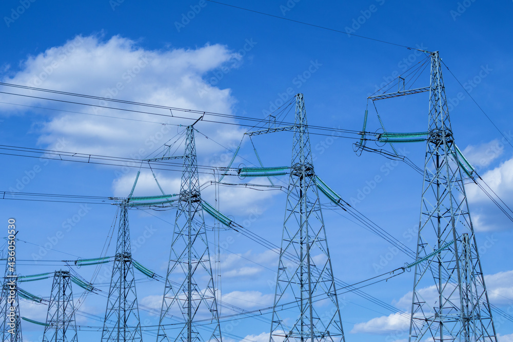 Six high voltage power towers against a backdrop of blue sky and cumulus clouds. Wires with insulators are connected to metal structures. Part of a global industrial network. Delivery of electricity.