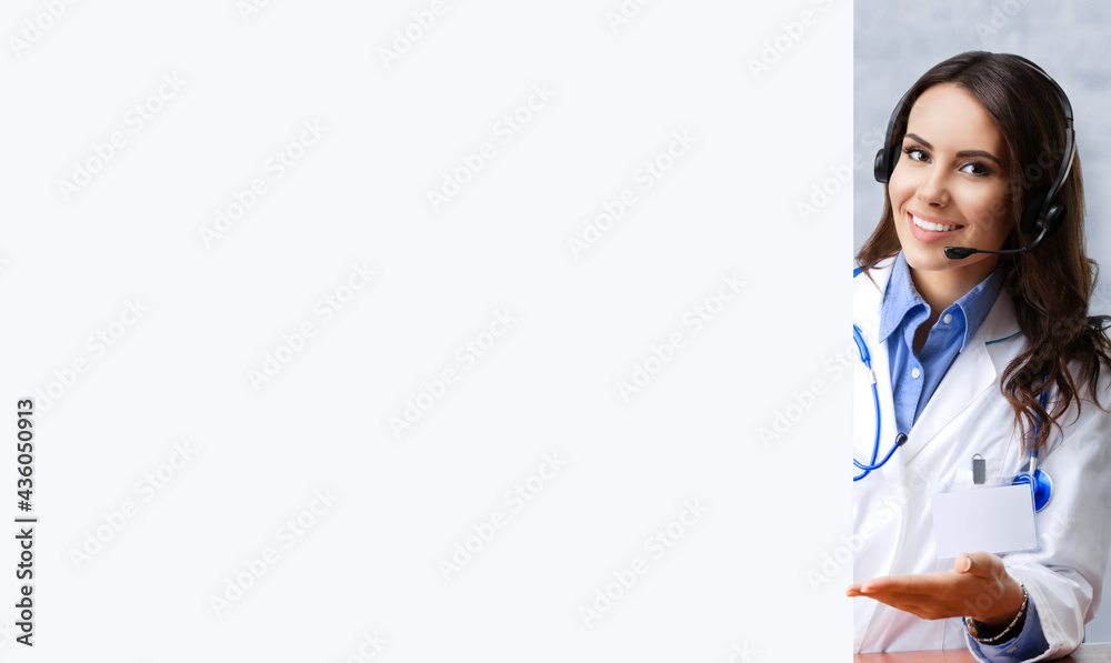 Portrait of smiling female doctor in headset holding, showing blank signboard with copy space, over office white brick loft wall. Medical call center concept. Portrait of smiling female doctor in headset holding, showing blank signboard with copy space, over office white brick loft wall. Medical call center concept.