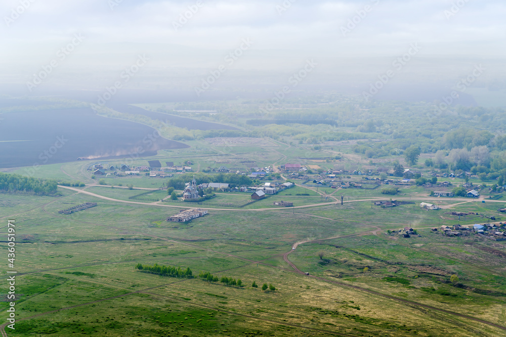 View from the mountain to the Russian village with a church and fields through a foggy haze. Photo taken near Andreevka village, Orenburg region, Russia