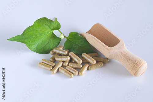 Herbal capsules on wooden spoon with herb leaf on white