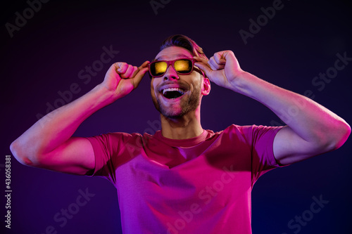 Portrait of attractive cheerful amazed guy looking far away touching specs having fun isolated over dark neon purple color background