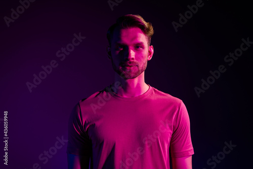 Portrait of attractive serious content guy wearing t-shirt isolated over dark neon light violet color background