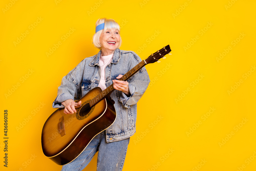 Fototapeta premium Photo portrait of elder woman playing acoustic guitar on festival feeling young isolated vivid yellow color background