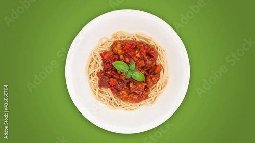 Rotating spaghetti bolognese on white plate against green background, top view, seamless loop, 4k