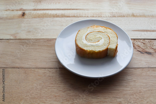 Cream roll cake sweet slice in white plate, delicious dessert isolated on wooden background closeup.