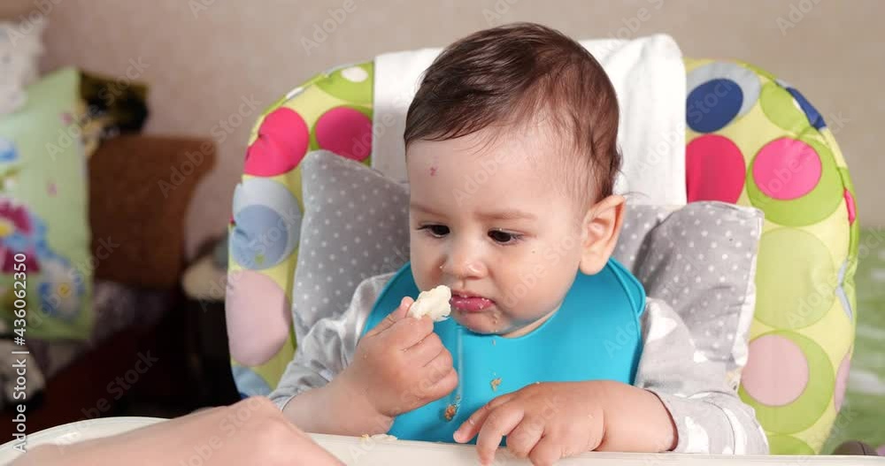 Mom feeds the boy with a spoon and hand, family food and parenthood concept. first complementary foods and self-feeding Mom feeds the boy with a spoon and hand, family food and parenthood concept. first complementary foods and self-feeding