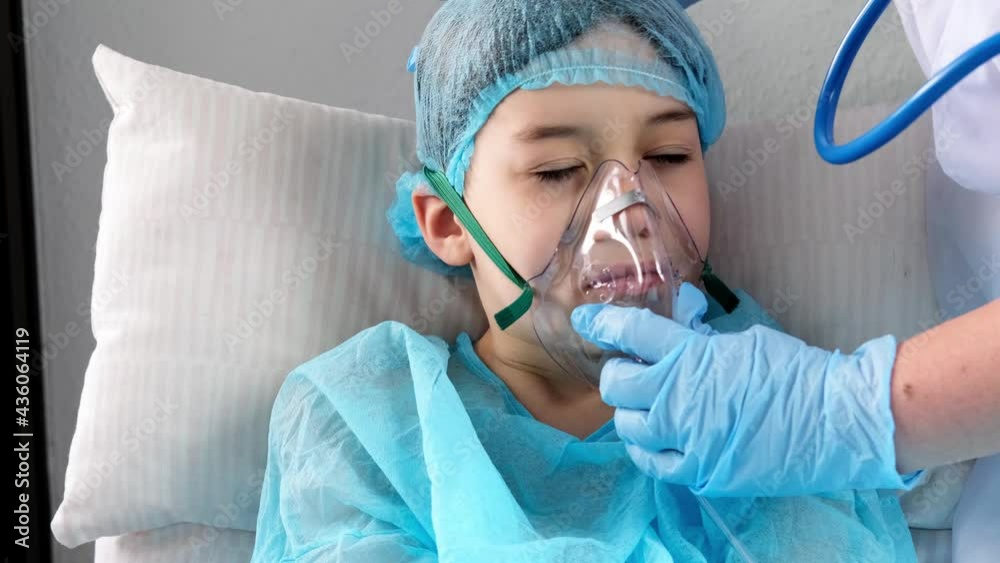 little patient in blue shirt, child, boy lies, doctor puts on facial oxygen mask, concept of medical care, anesthesiology, intensive care, oxygen therapy, treatment of coronavirus, COVID-19, surgery