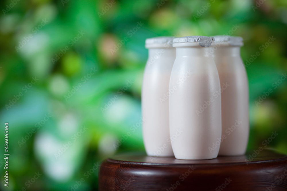 Natural liquid yogurt with probiotics in small plastic bottles on wooden table on background of green trees. Natural liquid yogurt with probiotics in small plastic bottles on wooden table on background of green trees.
