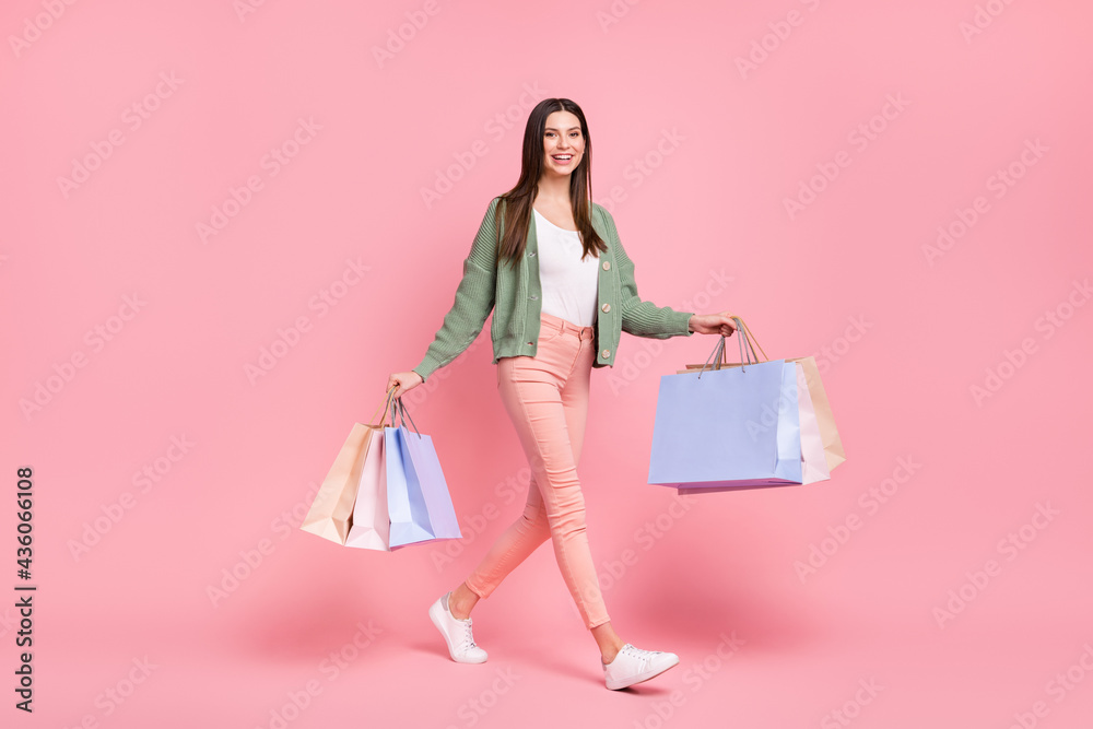 Full size photo of nice girl go with bags wear sweater trousers sneakers isolated on pink color background