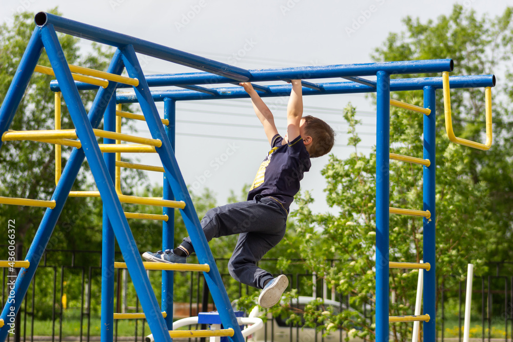 A little caucasian athletic boy climbs on the horizontal bars on the playground. A sporty child does exercises on the monkey bars in kindergarten. Children's sports and activities. Healthy lifestyle