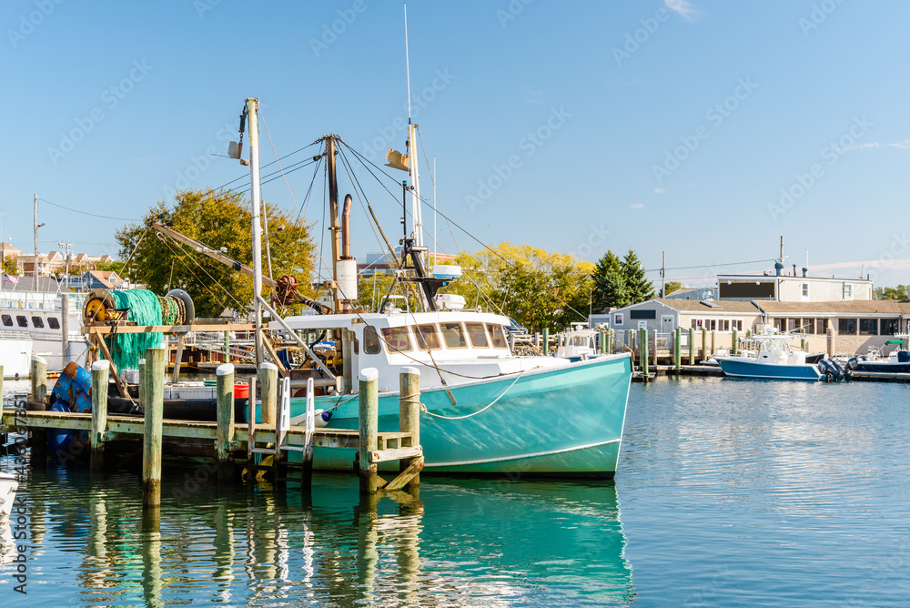 Fishing boat tied up to a wooden pier in a harbour on a sunny autumn day. Reflection in water