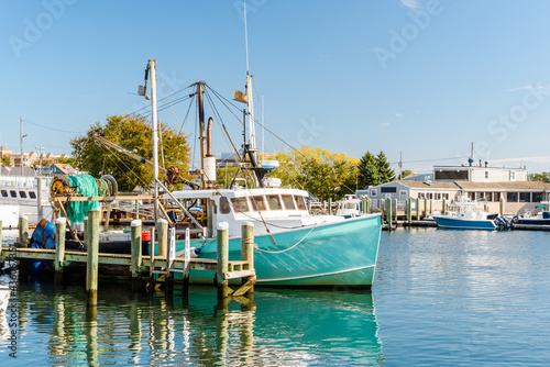Fishing boat tied up to a wooden pier in a harbour on a sunny autumn day. Reflection in water photo