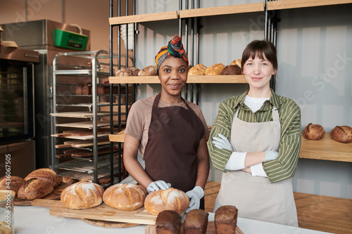 Portrait of two saleswomen in aprons standing near the table with homemade bread in the bakery shop photo