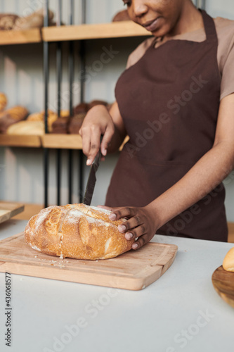 African woman in uniform cutting fresh bread on cutting board in the bakery