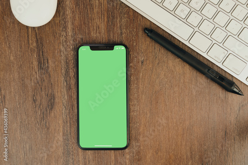 Fotografie Green Chroma Key on smartphone screen on wooden background with a computer beside it