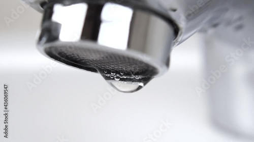 Water droplets drip from an unclosed leaky tap with a strainer in slow motion. Fluid leaking from stainless steel faucet with mesh filter. Macro shot. Economy and ecology concept photo