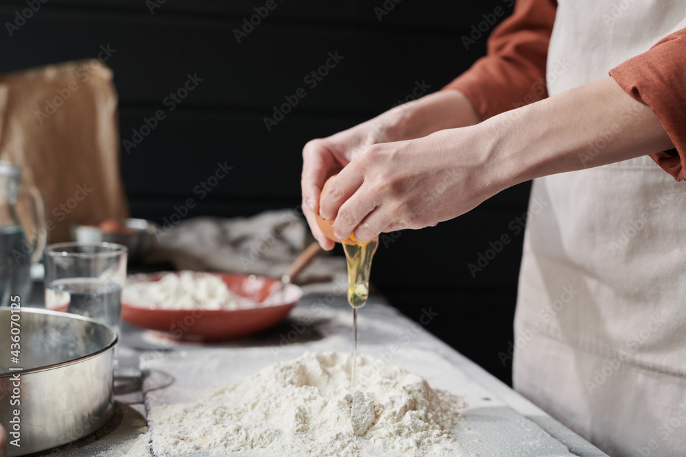 Close-up of woman adding egga and making a dough while baking the pie in the kitchen