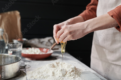 Close-up of woman adding egga and making a dough while baking the pie in the kitchen
