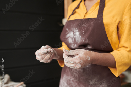 Close-up of young woman with flour on her apron and on her hands cooking in the kitchen