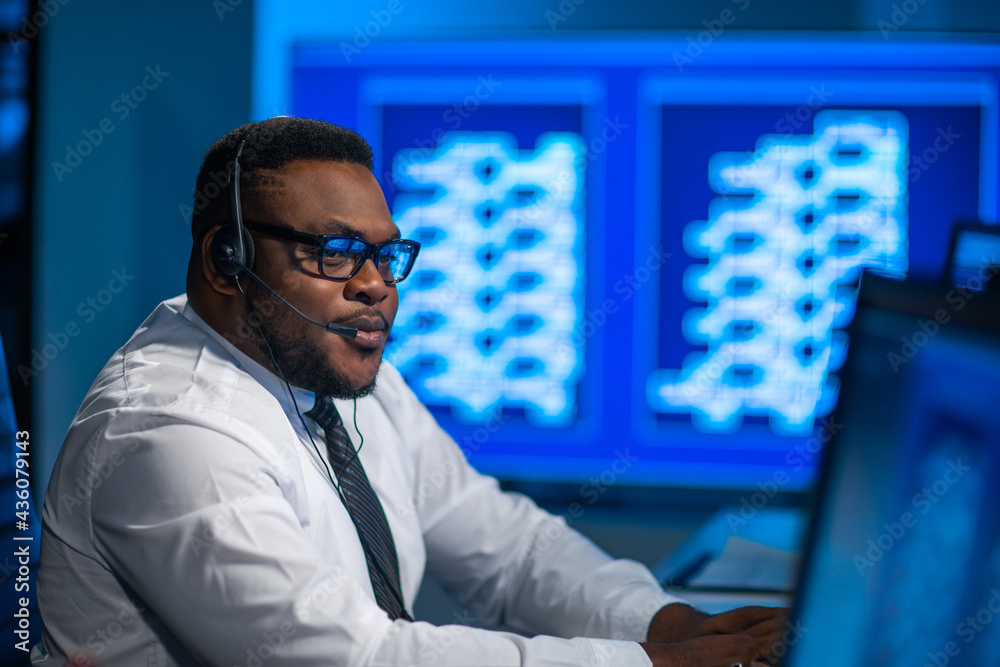 Call-center worker is speaking with the client by headset. Workplace of the african-american support operator. Call-center worker is speaking with the client by headset. Workplace of the african-american support operator.