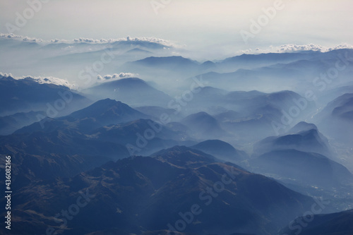 Aerial view of misty mountains and clouds above the mountain peaks, blue tinted