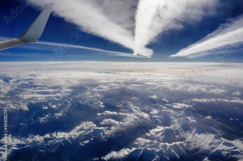 Aerial view of snowy mountains, clouds and plane trails, opposite the sunlight