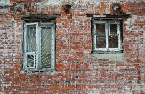 Old red brick wall, white paint and embossed walled up windows with white bars.