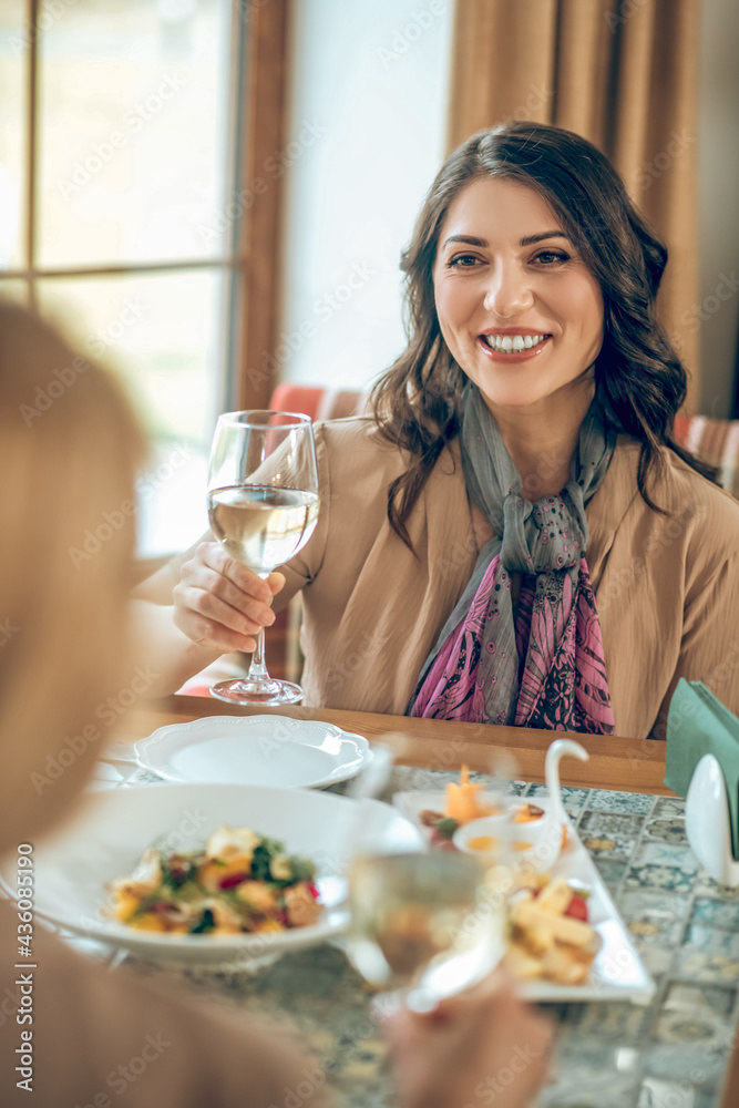Smiling young woman holding a glass of wine and toasting with friends