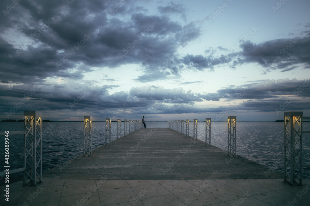 A lonely man on a marina under a beautiful dramatic sunset sky. 