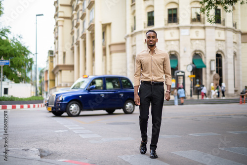 African businessman outdoors in city smiling and walking full body shot