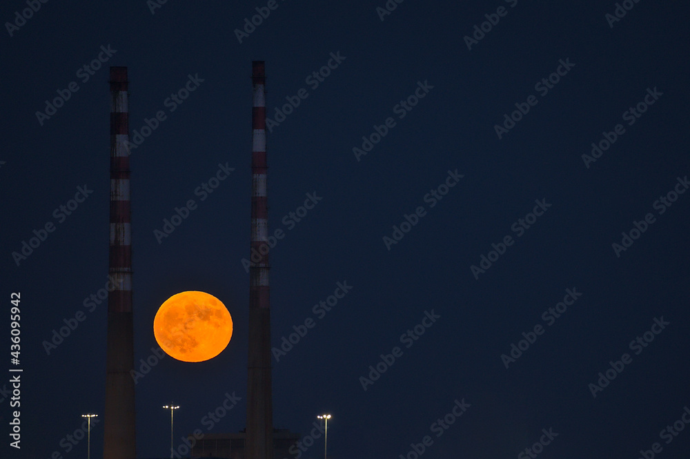 Beautiful view of red super flower Moon rise in the Irish sky between iconic Poolbeg Generating Station (Poolbeg CCGT) chimneys on May 26, 2021 seen from Dublin City Motocross Track, Dublin, Ireland