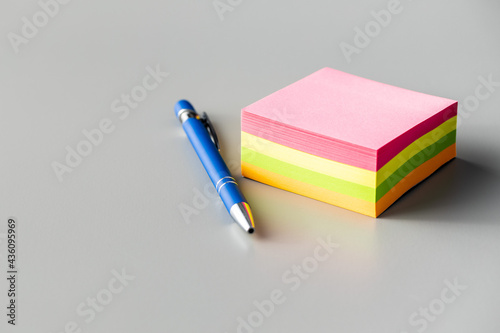 Blank sticky paper notepad and pen on gray table.